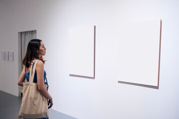 Young woman walking through a gallery and looking at the canvas.