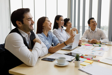 Group of five diversity businessmen, two men and three women sitting at meeting desk and pay attention with satisfied laugh for speaker of the conference.