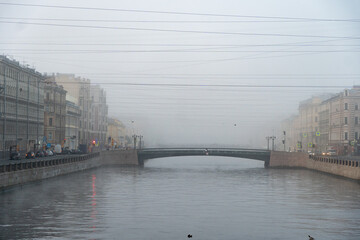 St. Petersburg, Russia - November 1, 2020: dense tumar in St. Petersburg, a canal drowning in haze, a pedestrian and automobile bridge, an embankment, gray sky with wires