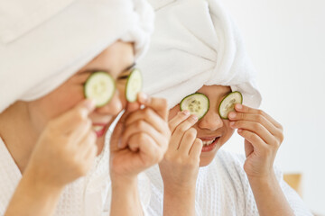 A little girl and beautiful mother wearing spa dress playing with pieces of cucumber for treatment with joy and happy manner. The idea for health care and relaxing and family relationship