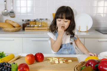 A cute 3 years Asian girl testing pieces of fruits in kitchen