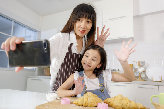 A cute and beautiful mother with young and little daughter, 7 years old, taking a selfie photo with a smartphone in modern kitchen. Concept love and relationship of family.