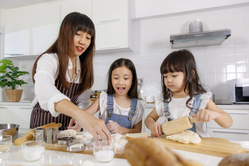 Family group photo of 30s mom teaching and educate two little girls, 3 years and 7 years old, how to make bread and bakery. They are learning and playing with flour in a modern kitchen