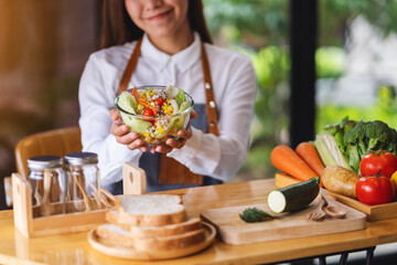 Closeup image of a female chef cooking and holding a fresh mixed vegetables salad in kitchen