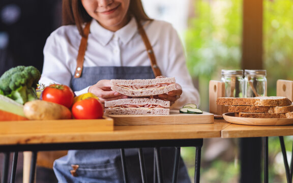 Closeup image of a female chef cooking and holding a piece of whole wheat ham cheese sandwich in kitchen