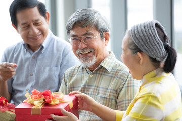 Senior Asian people joining together and give the gift boxes to each other and the man feels excited.  Concept for happy lifestyle and good relationship with older people