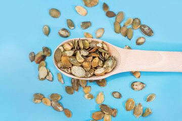 peeled pumpkin seeds in a wooden spoon on a blue