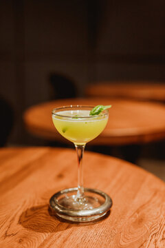 A sour cocktail in a coupe glass with a basil leaf garnish. Lifestyle vertical image. Selective focus.