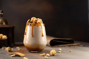 Tuinposter Sweet Milkshake with caramel syrup,cream liqueur,caramel popcorn and chocolate powder on brown background with vintage,manual coffee grinder. © Olga_arisphoto