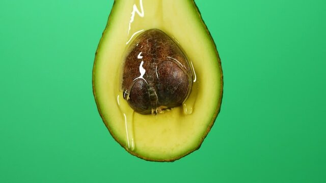 Slow motion close-up of fresh avocado fruit and oil flowing on green background