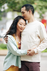 Obraz premium Happy young Chinese couple in love in casual clothes standing outdoors, hugging and closing eyes