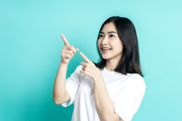 Obraz premium Beauty smiling brunette Asian woman pointing away and smiling and looking at the camera over color background