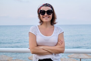 Smiling mature woman in sunglasses looking at camera with crossed arms