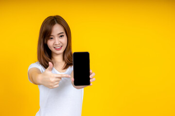 Naklejka premium Smiling young Asian woman is pointing on smartphone standing on yellow background.