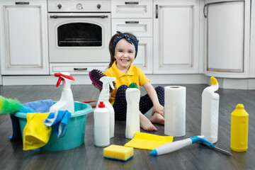 Little girl plays with detergents and a brush on the kitchen floor while cleaning.