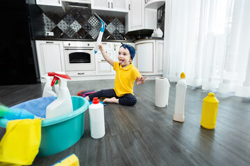 Little girl plays with detergents and a brush on the kitchen floor while cleaning.