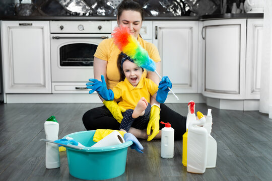 Beautiful young woman and her little daughter sit on the floor and have fun cleaning their house