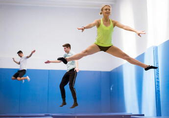 Fototapeta premium Young athletic woman practicing side split in jump on trampoline in sports center..