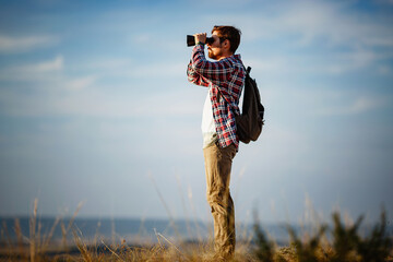 Guy looking at binoculars in hill. man in t-shirt with backpack.