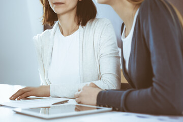 Businesswoman giving presentation to her female colleague while they sitting at the desk with computer. Group of business people working in office. Teamwork concept