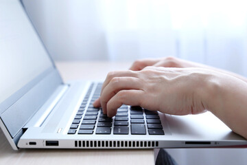 Female hands on laptop keyboard on a desk in sunlight. Woman types on the laptop keyboard sitting...