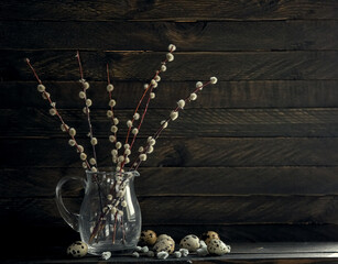 A bouquet of willow with flowers in a dark vase on a dark background.