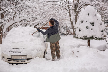 A man cleans the car from snow in winter.