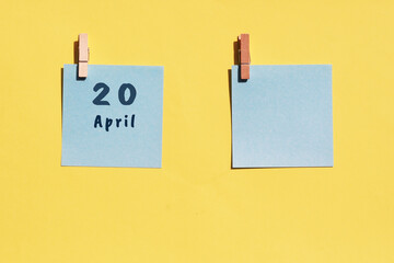 April 20st. Day of 20 month, calendar date. Two blue sheets for writing on a yellow background. Top view, copy space. Spring month, day of the year concept