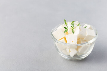 Diced feta cheese garnished with thyme in glass bowl on gray background, horizontal, copy space