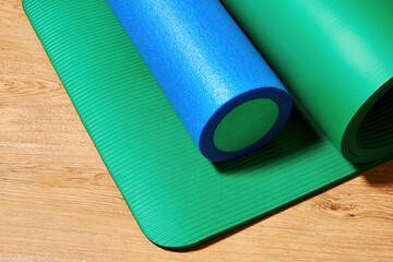 Green fitness mat and roller on the wooden floor. Sports and pilates backgrounds