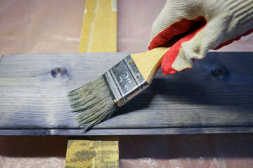 Handling a woody pine plank with a dark mordant with a paintbrush for deeply impregnating wood for...