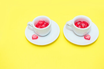 two cups with hearts on a red background. the view from the top. red hearts spilled out. isolated on a yellowbackground. copy space. panton