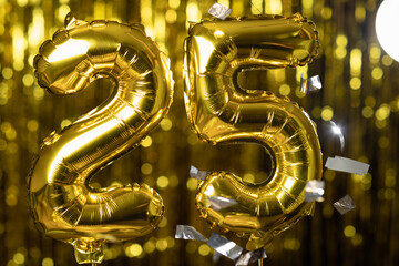 Golden number 25 twenty five made from an inflatable balloon, on a yellow background. One of the...