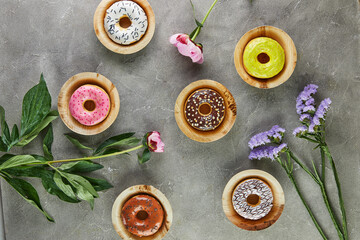 Fototapeta na wymiar Multicolored donuts with glaze and splashes with flowers on a gray background