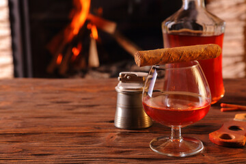 A glass of brandy and a cigar on the background of a burning fireplace