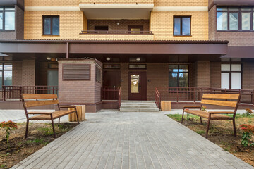 Entrance in new modern high-rise residential building with paving stone walkway and benches on both sides