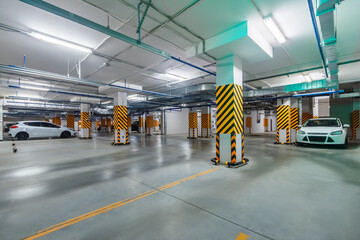 Inside view of bright and clean underground parking garage with cars in basement of high-rise...