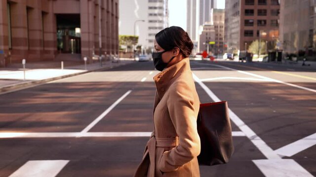 Mixed Ethnicity (Asian-African) Business Woman Wearing A Face Mask Walks Across The Street In Downtown Los Angeles.