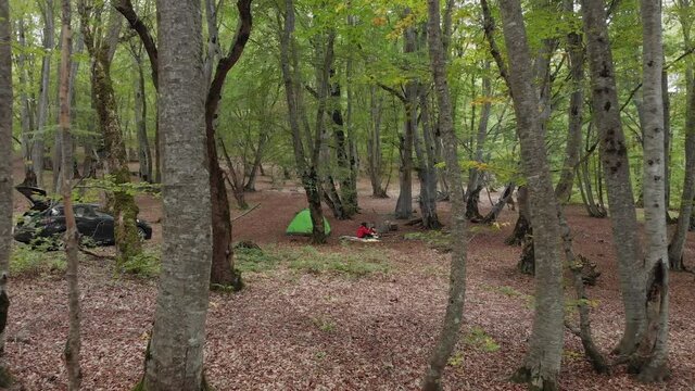 Aerial view of female person by the fire alone camping outdoors with tent and car standing. Singlehood and human well being concept