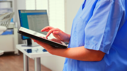 Close up of assistant holding tablet and analysing teeth digital radiography of patient standing in...