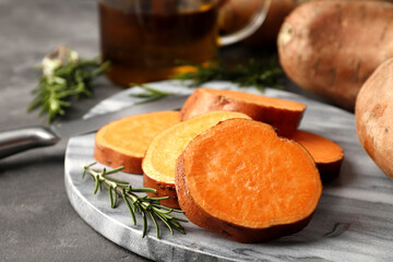 Composition of fresh sliced sweet potatoes, rosemary spices, knife and vegetable oil close-up.