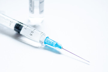 Syringe with needle without cover or top, vial or phial on a white empty space background ready to be used. Covid or Coronavirus vaccine or monoclonal antibodies background, close up