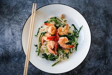Stir-fried rice vermicelli and water mimosa with prawns on white plate with chopsticks.