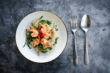 Stir-fried rice vermicelli and water mimosa with prawns on white plate with cutlery.