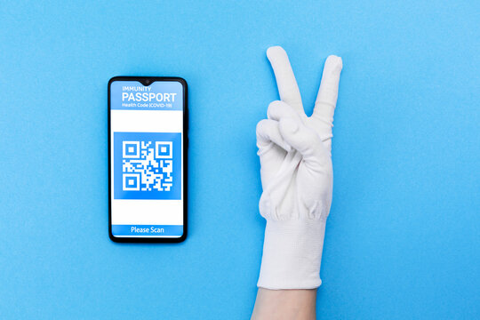 Hand in gloves and electronic Immunity passport with a COVID-19 vaccination stamp and qr-code on a smartphone screen on the blue background. Flat lay. Concept of vaccination and digital passport