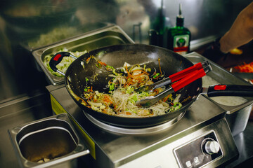 cooking vegan wok noodles with vegetables in cafe kitchen