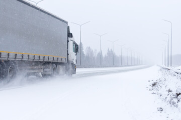A heavy-duty car drives along the motorway in winter during a snowstorm.