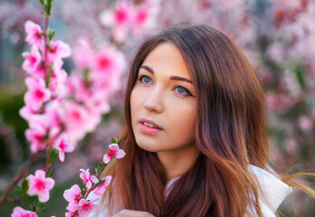 Naklejka premium Smiling beautiful girl standing near a peach tree during sunset. Happy face. Spring time.