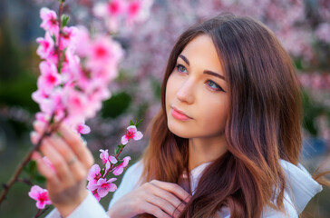 Fototapeta premium Smiling beautiful girl standing near a peach tree during sunset. Happy face. Spring time.