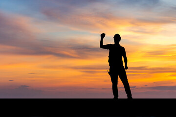 Silhouette of Factory worker man with clipping path in hard hat with celebrating victory, young man celebrates with hand in the air sunset background